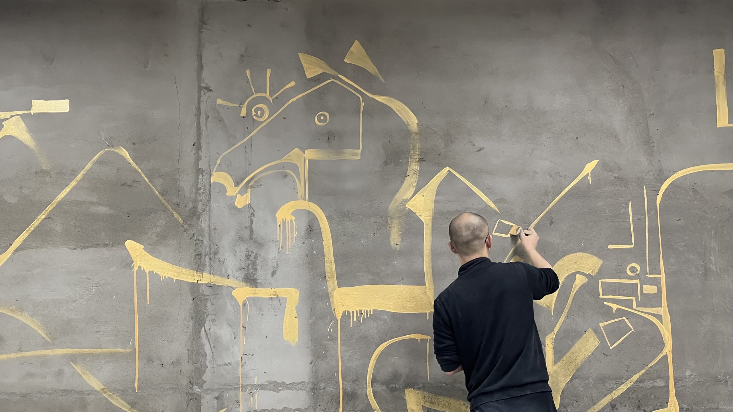 Lu Renjie painting bronze-script figures in gold on a raw concrete wall